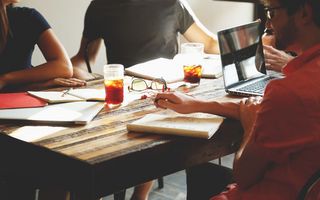 Drei Personen sitzen an einem Tisch mit Unterlagen und Laptops